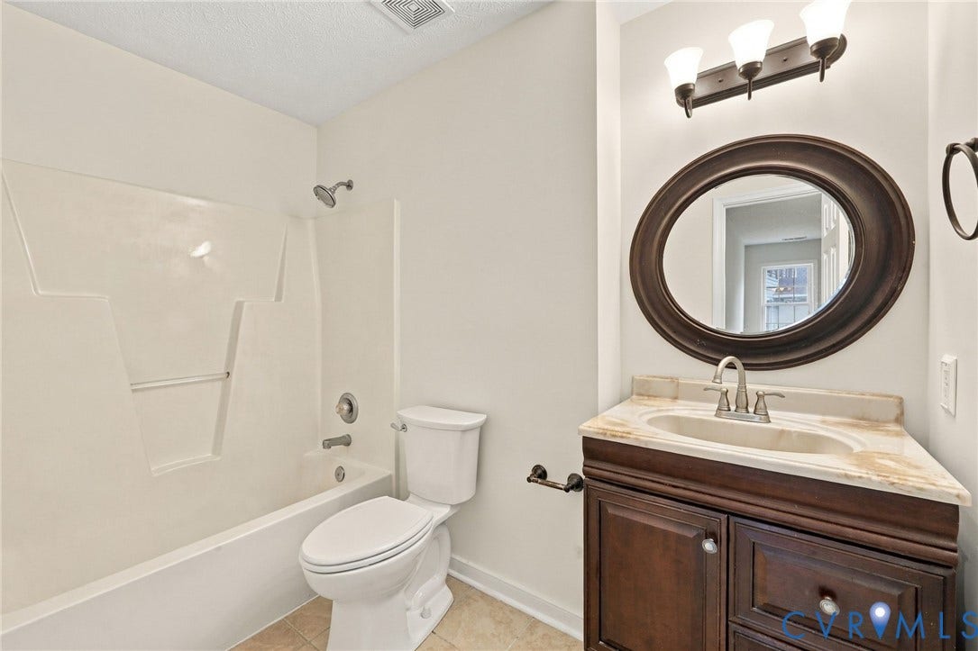 Bathroom featuring a vanity with a stone-finish countertop, an oval mirror, a three-light fixture, a toilet, and a tub-shower combination
