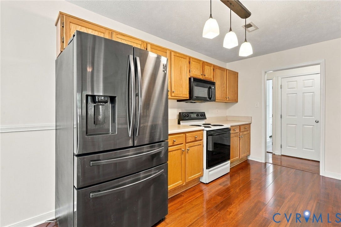 Kitchen featuring wood-finish flooring, stainless steel French door refrigerator, black microwave, black electric range, and light wood cabinetry