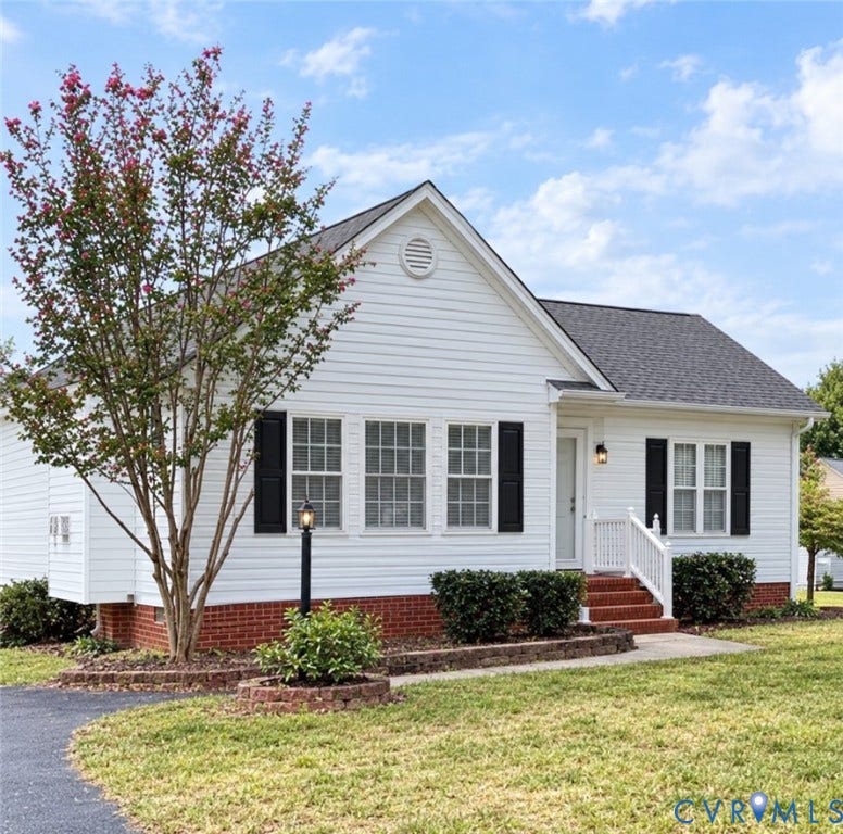 White siding exterior with black window shutters, brick foundation, a front porch with white railing, and a mature flowering tree. Photo enhanced by AI