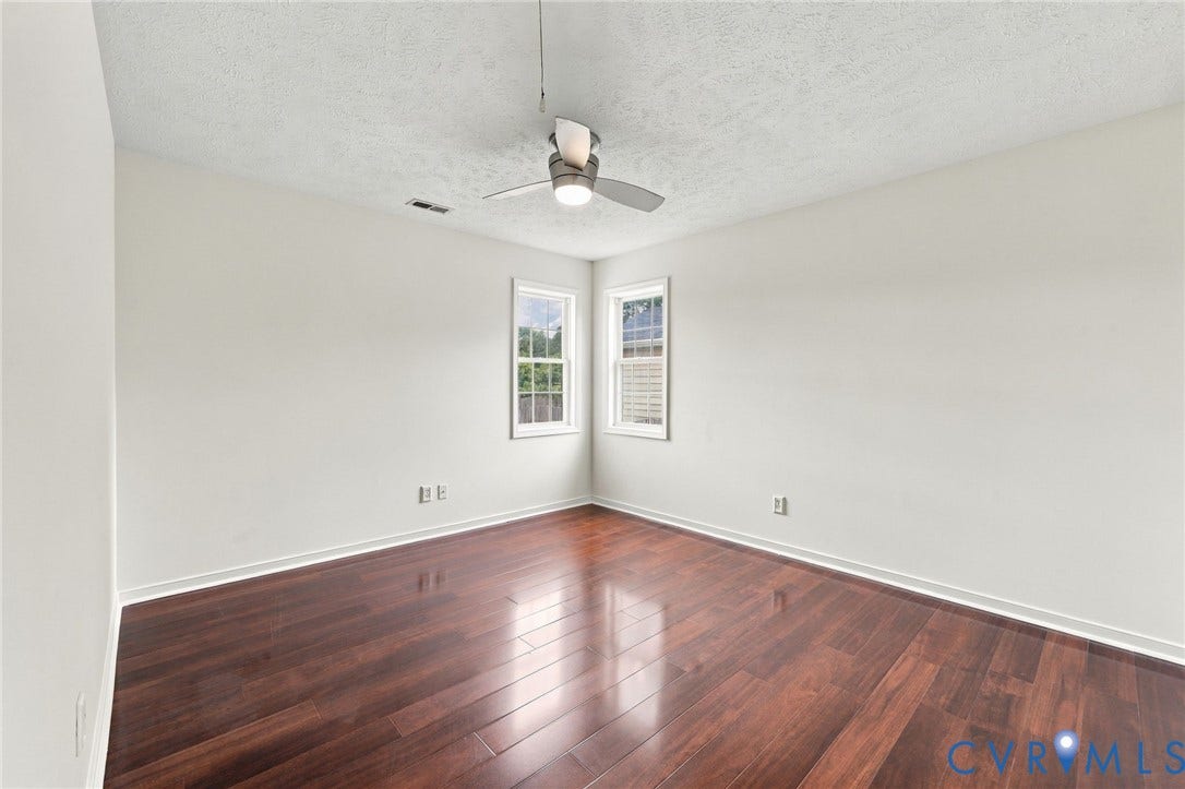 Wood-finish flooring, white walls, two windows, and a ceiling fan with integrated lighting