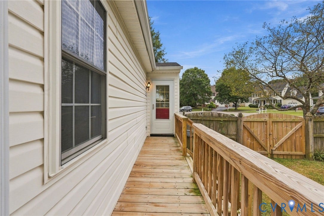 Exterior featuring light-colored siding, a wooden ramp with railings, an exterior light fixture, and a window with grilles