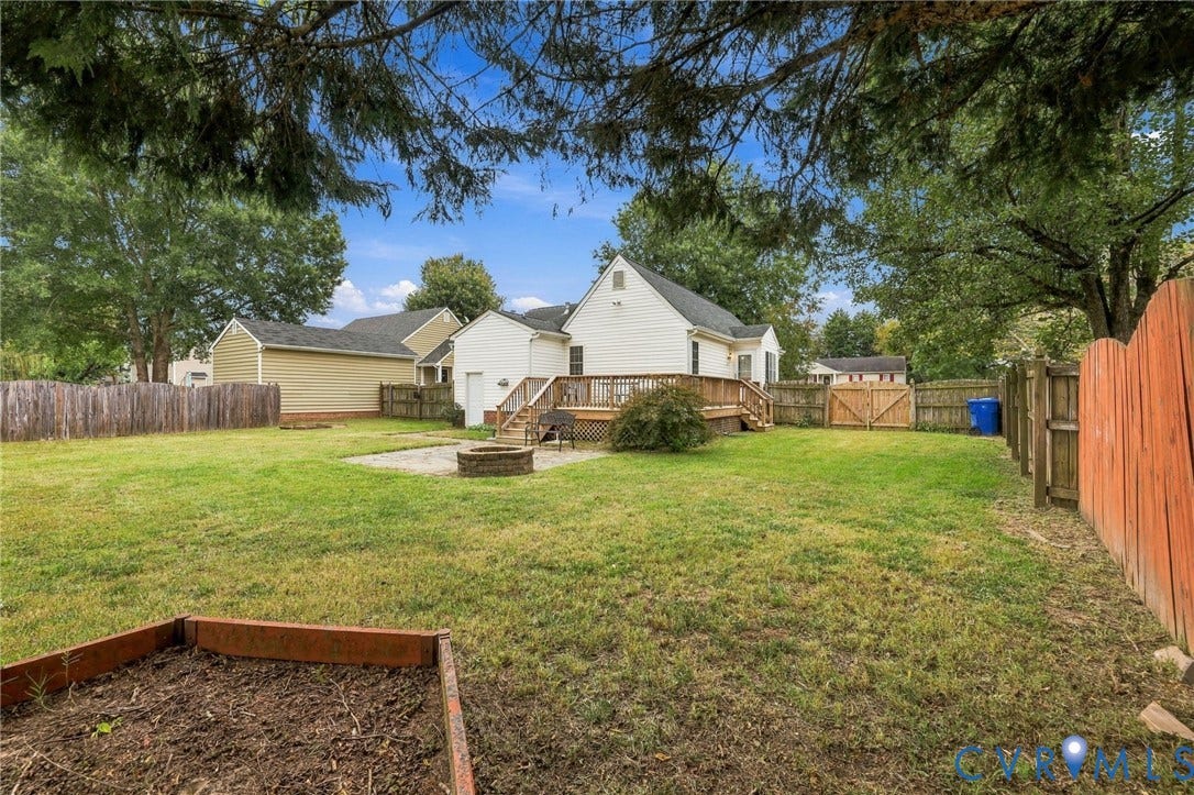 Expansive backyard featuring a spacious wood deck, stone patio, and a raised garden bed