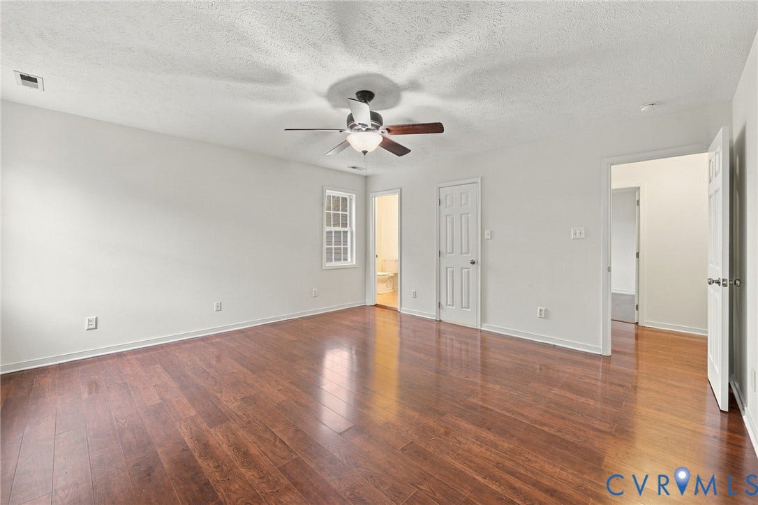 Spacious room with wood-finish flooring, light-colored walls, ceiling fan, and multiple doorways