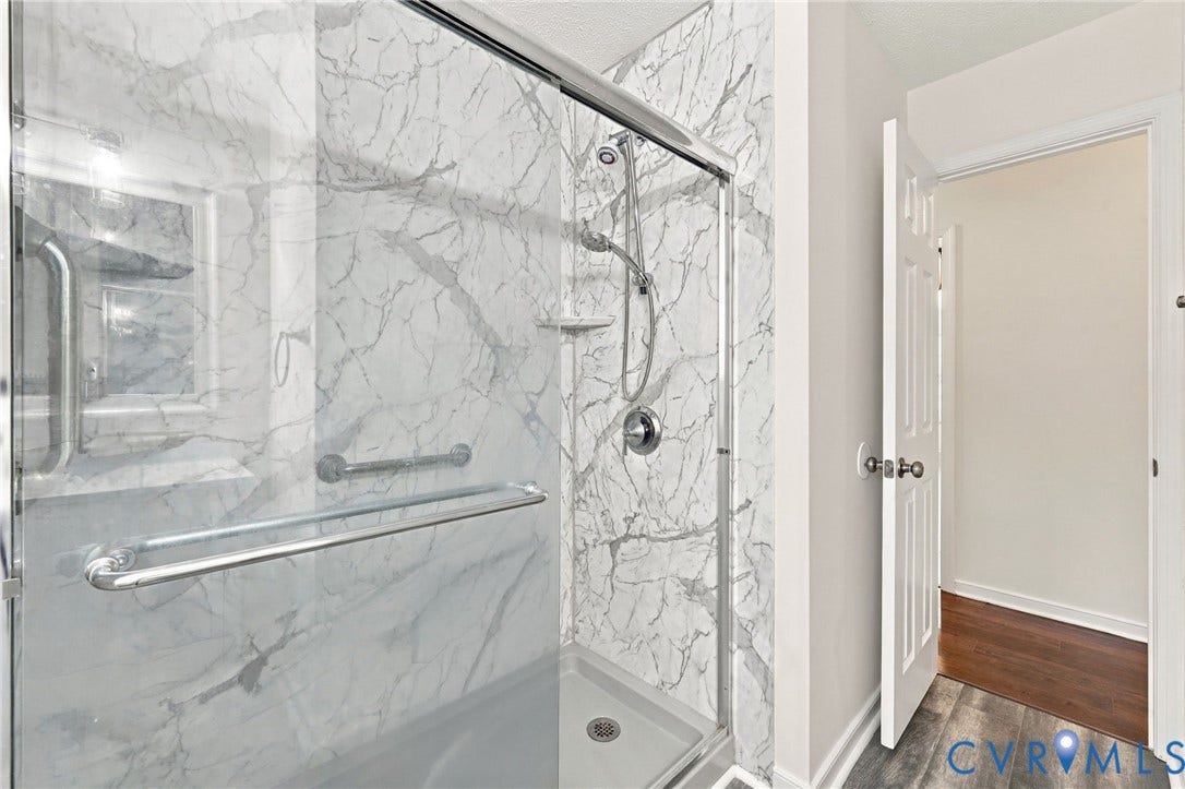 Walk-in shower with marble-look surround, chrome fixtures, and a glass enclosure