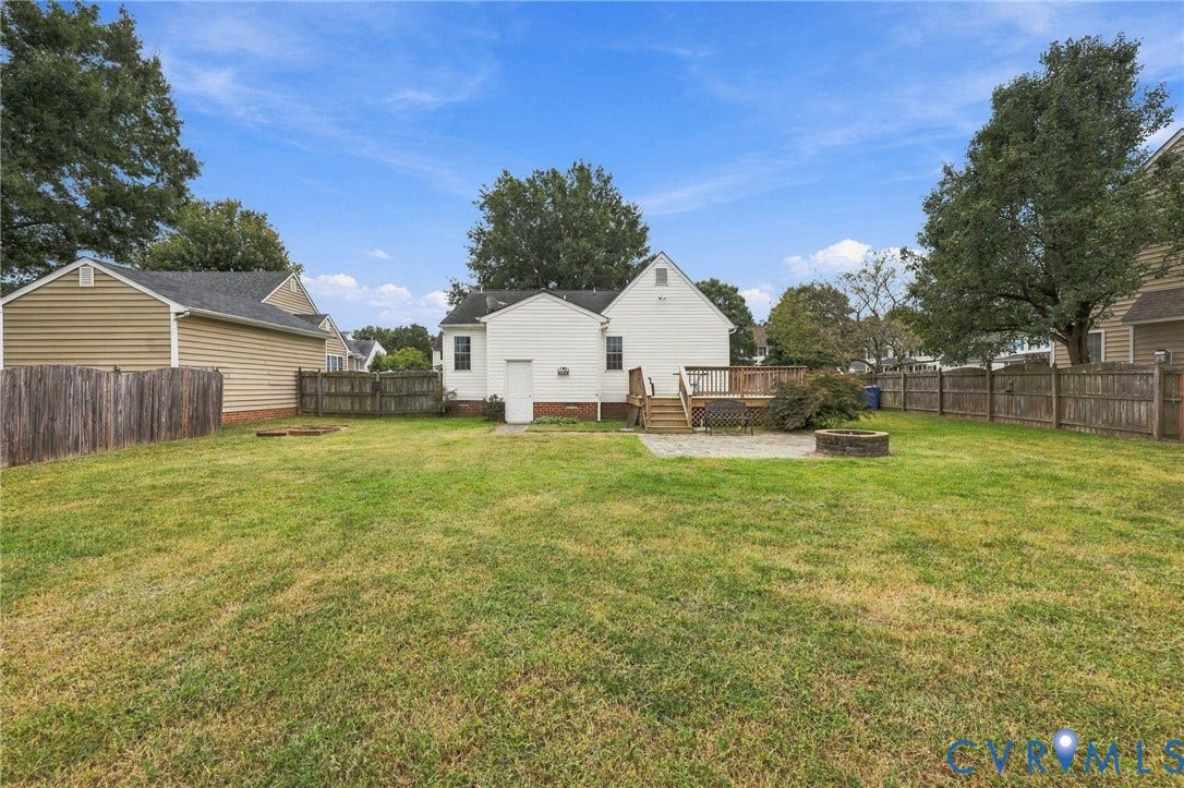 Expansive backyard featuring a wood-tone privacy fence, a multi-level wood deck, and a paver patio with a built-in fire pit