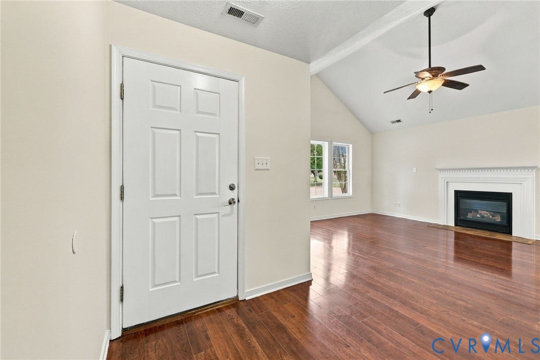 Vaulted ceiling, wood-finish flooring, fireplace with white mantel, ceiling fan, and multiple windows