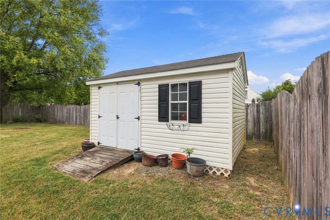 White vinyl-sided shed with double entry doors and a single window with black shutters