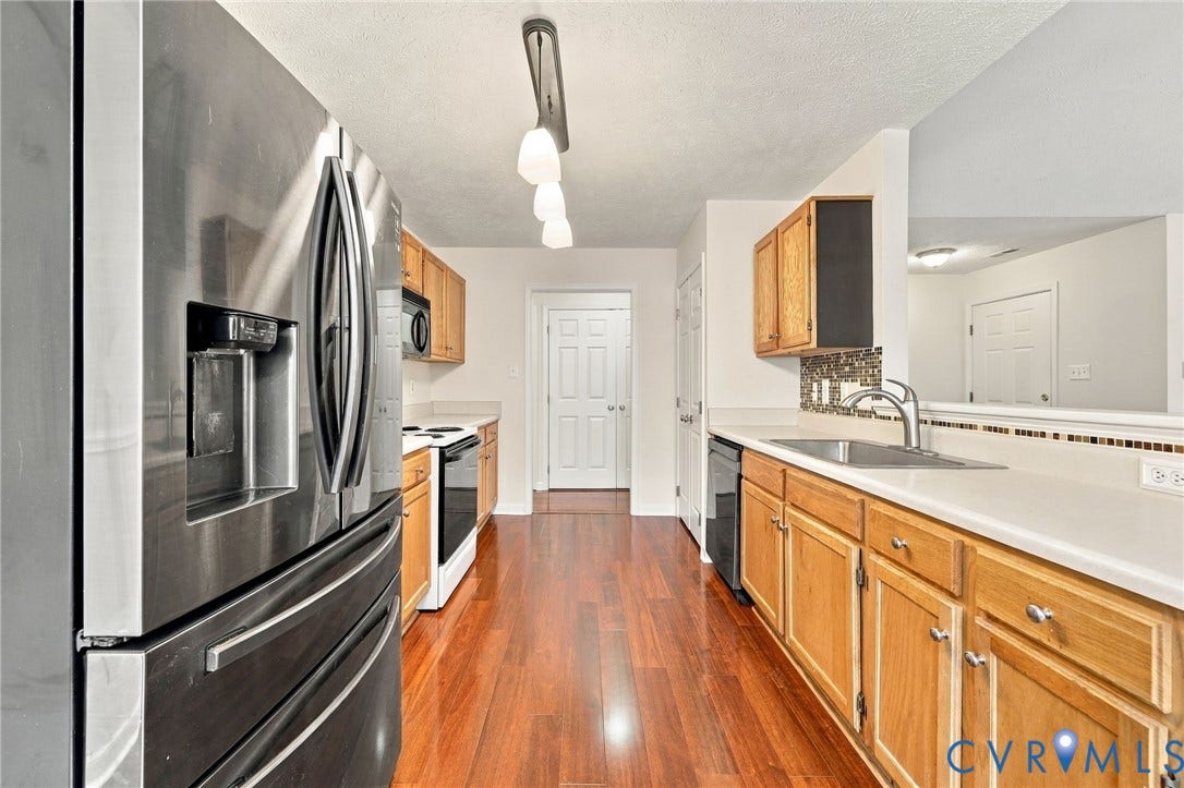 Kitchen featuring wood-finish flooring, stainless steel appliances, light wood cabinetry, a tiled backsplash, and light countertops