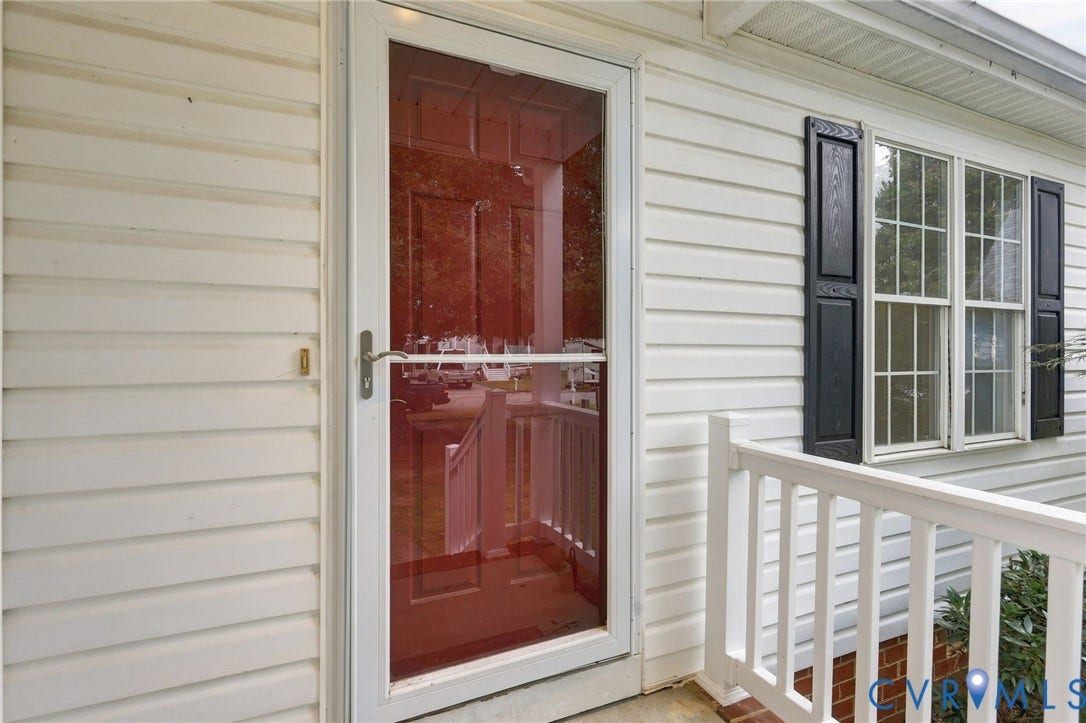 White vinyl siding exterior with a storm door, multi-pane windows, and decorative black shutters