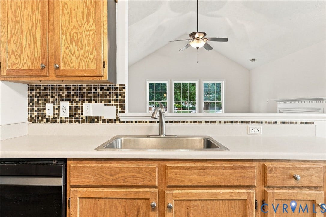 Stainless steel sink with a gooseneck faucet, light-toned countertops, wood-finish cabinetry, and a mosaic tile backsplash