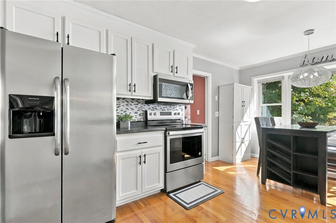 White cabinetry, stainless steel appliances, black countertops, hardwood flooring, and a decorative pendant light
