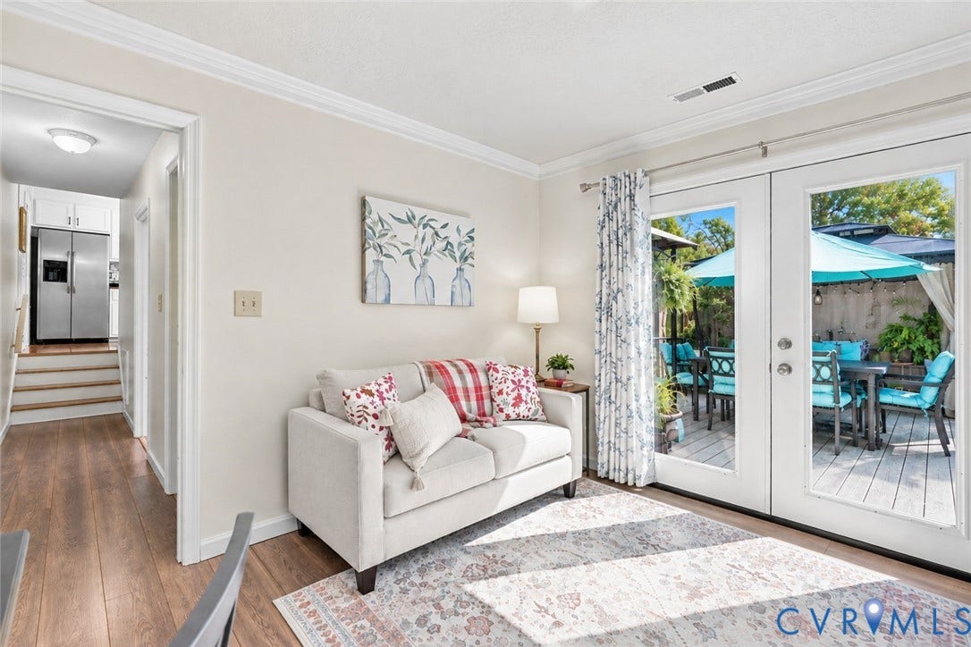 Wood-finish flooring throughout, white crown molding, and double glass-paneled doors opening to an outdoor patio with a privacy fence