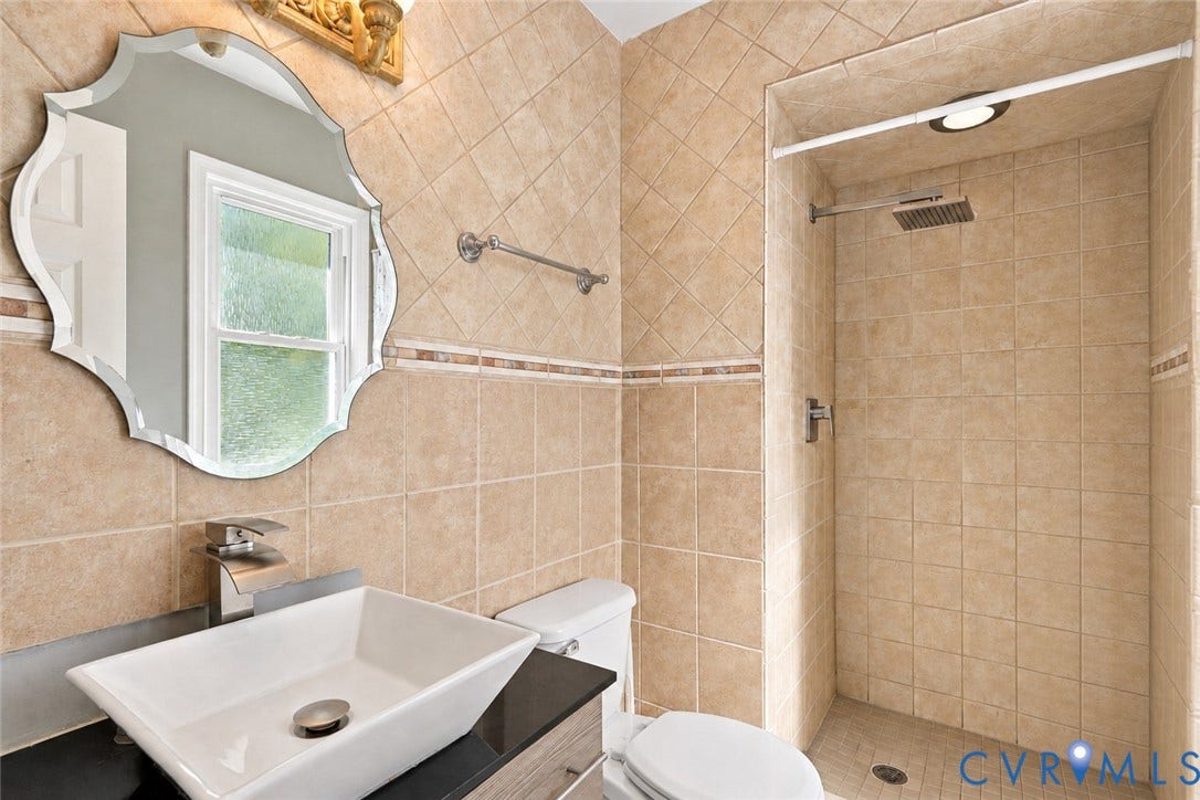Tiled bathroom featuring a vessel sink, chrome single-handle faucet, and an ornate framed mirror