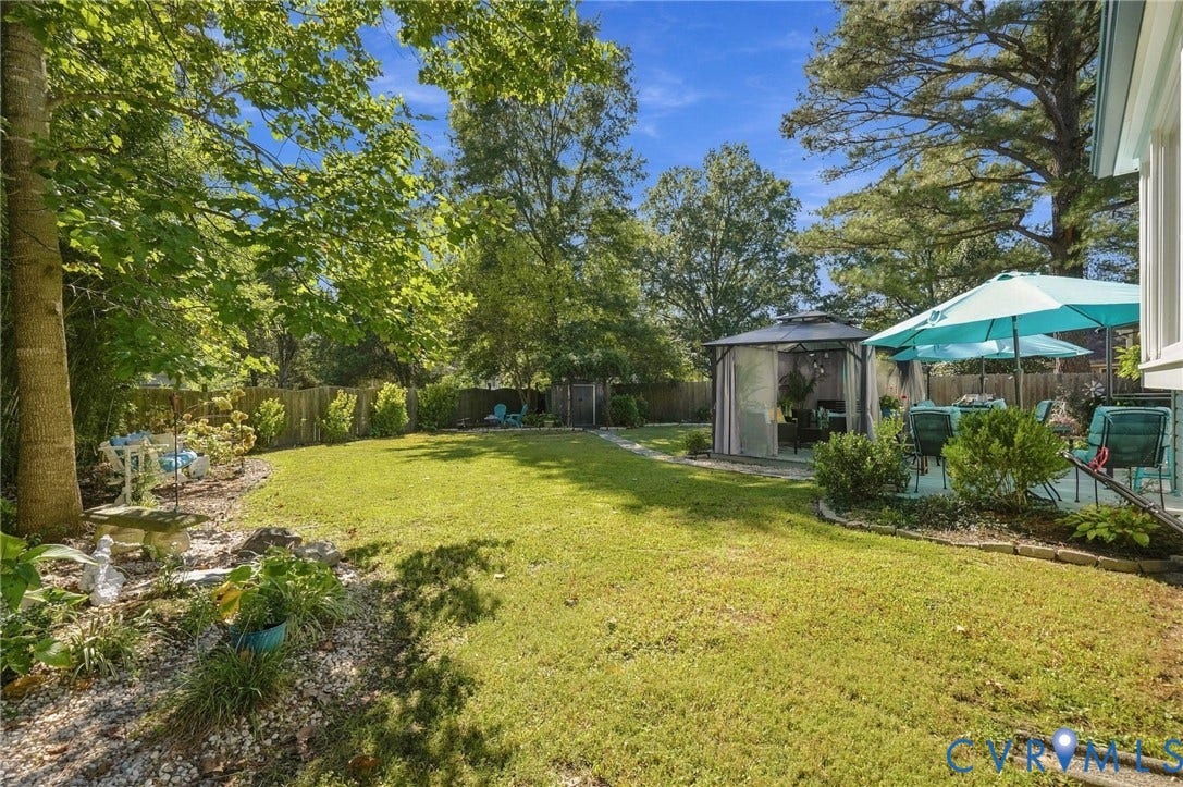 Expansive backyard featuring a manicured lawn, established trees, privacy fencing, and a dedicated patio area