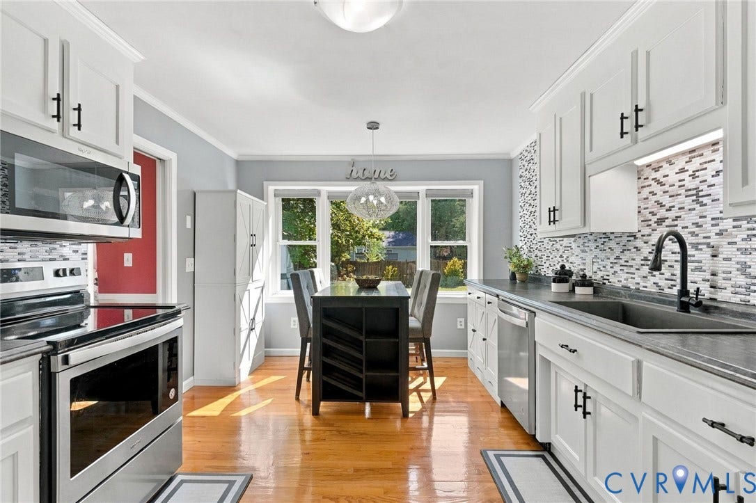 White shaker-style cabinetry with black hardware, mosaic tile backsplash, stainless steel dishwasher, farmhouse sink and hardwood floors