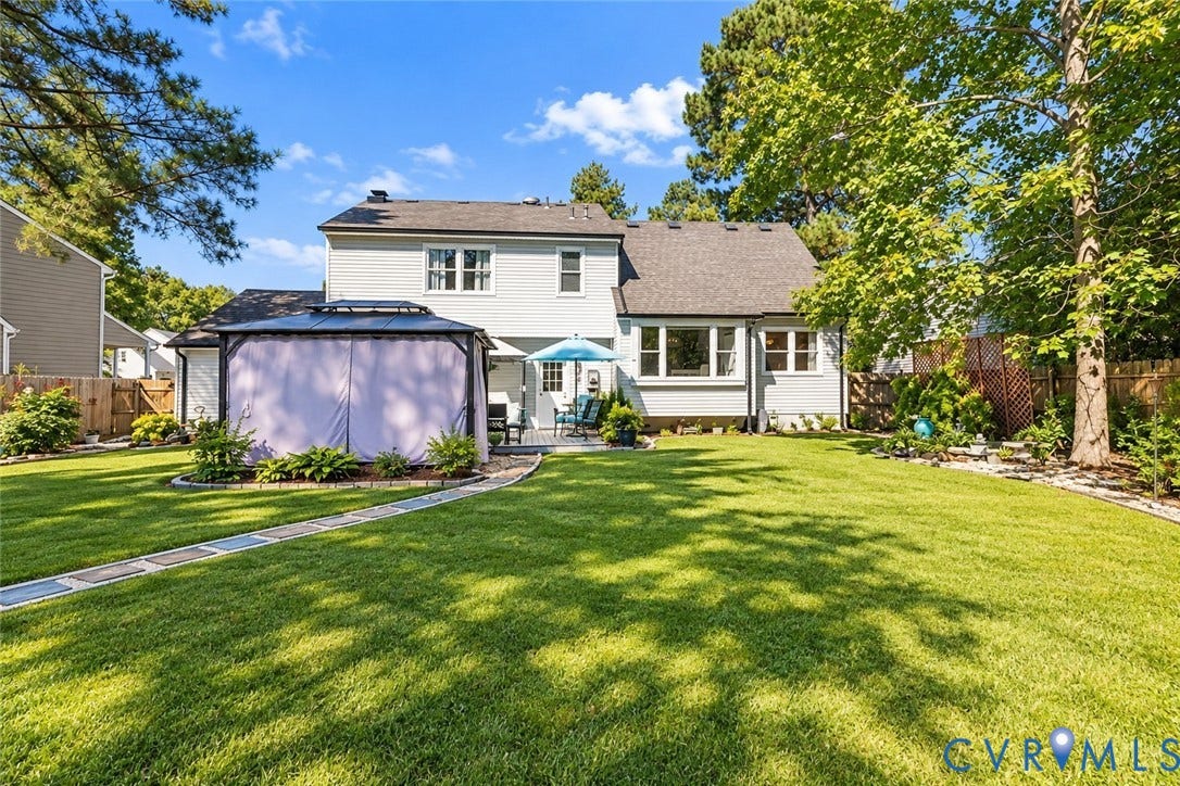 Expansive green lawn with a paved pathway, leading to a covered gazebo and a rear deck