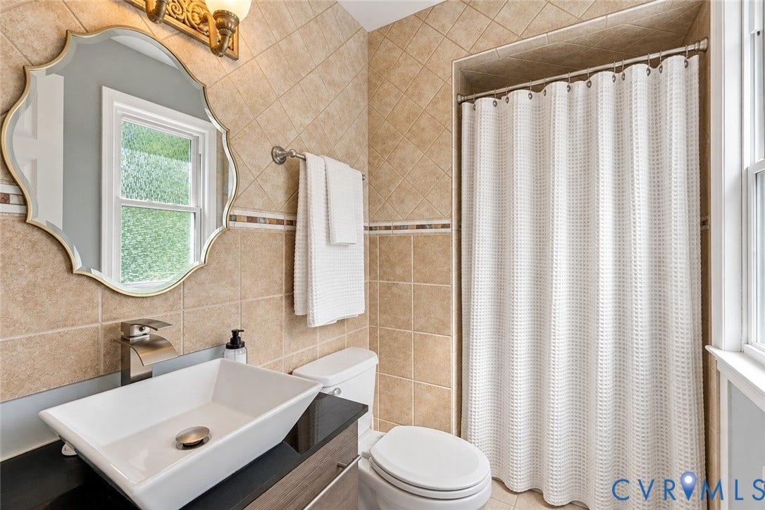 Bathroom featuring a vessel sink, dark countertop, and tiled walls with a decorative accent band