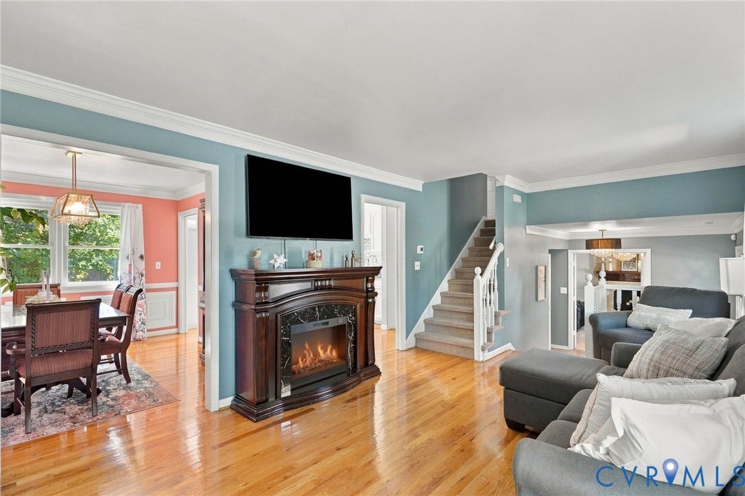 Spacious open-concept living area showcasing gleaming wood-finish flooring, a fireplace with decorative mantel and black surround, a wall-mounted flat-screen television, and a staircase with white railings