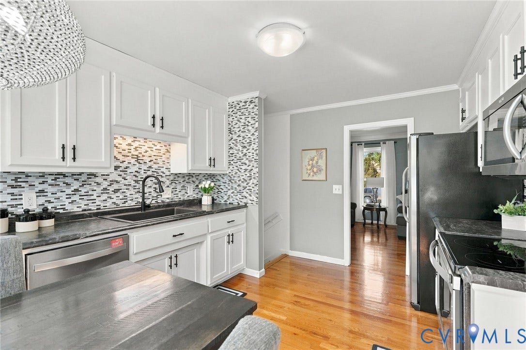 White shaker-style cabinetry with black hardware, mosaic tile backsplash, stainless steel dishwasher, farmhouse sink and hardwood floors