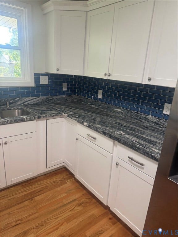 White shaker-style cabinetry, dark patterned countertops, blue subway tile backsplash, and wood-finish flooring