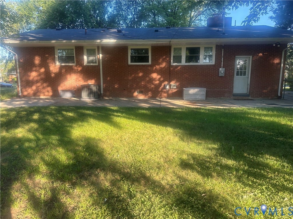 Brick exterior with multiple windows, a white rear entry door, and a level lawn area