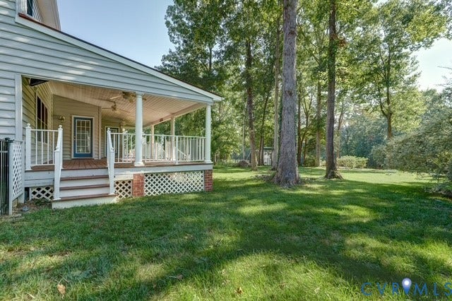 8113 Ainsdale Lane, Chesterfield, VA 23832 Expansive rear yard with mature trees and a covered deck featuring white railings, lattice skirting, and brick accents