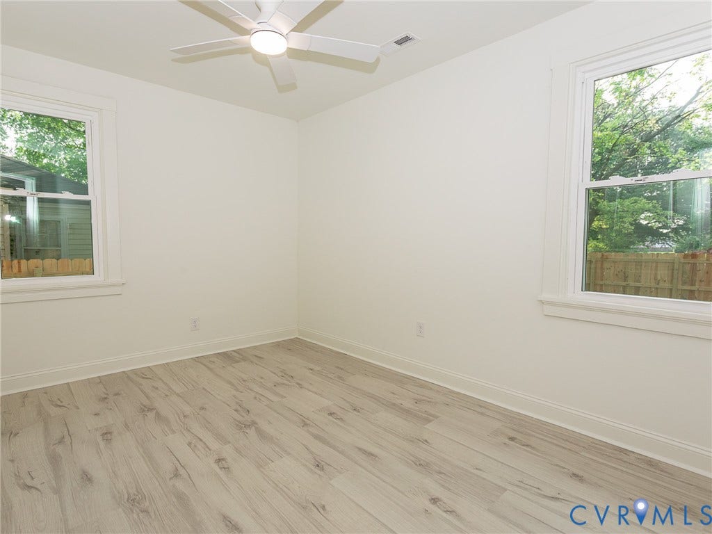 1601 N 25th Street, Richmond, VA 23223 Light-toned wood-finish flooring, white walls, two windows with white trim, and a ceiling fan with integrated lighting