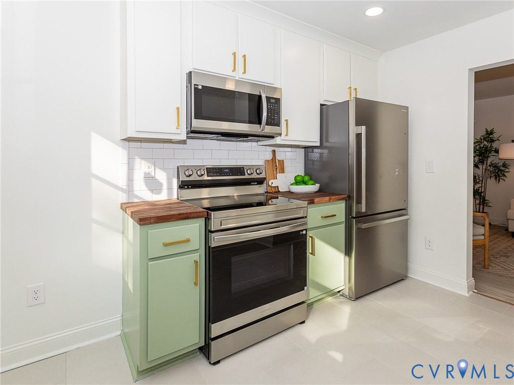 1601 N 25th Street, Richmond, VA 23223 White shaker-style upper cabinetry with gold-tone hardware, stainless steel appliances, butcher block countertops, subway tile backsplash, and light-toned flooring