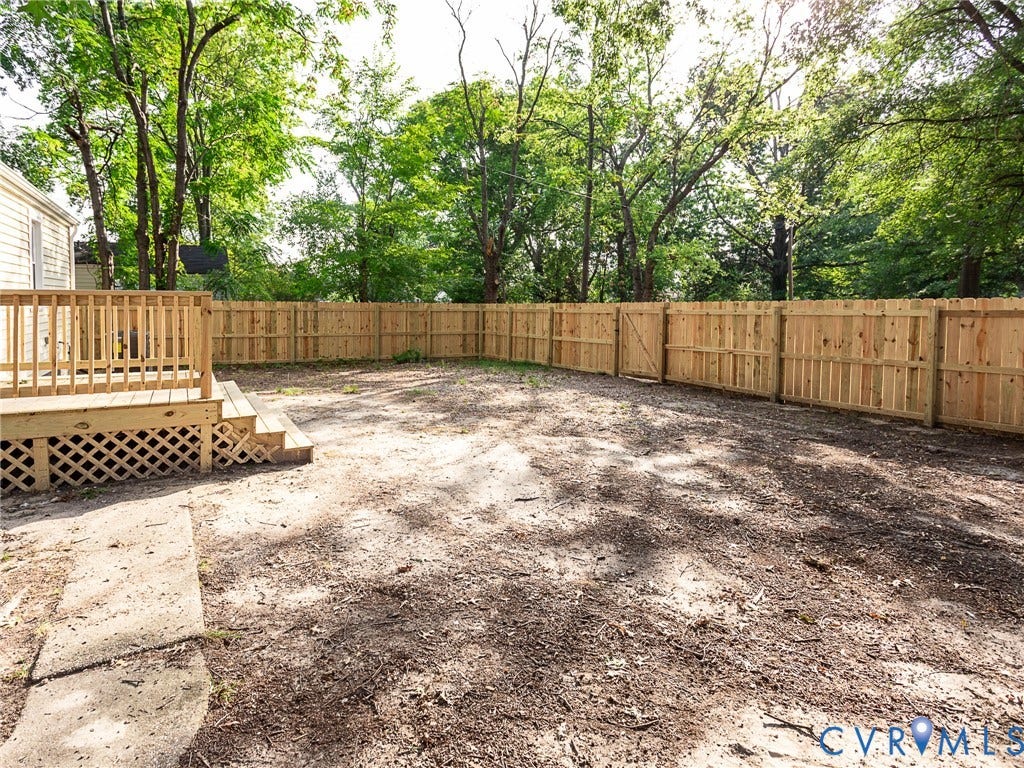 1601 N 25th Street, Richmond, VA 23223 Spacious backyard featuring a new wood privacy fence, a new wooden deck with railing, and mature trees