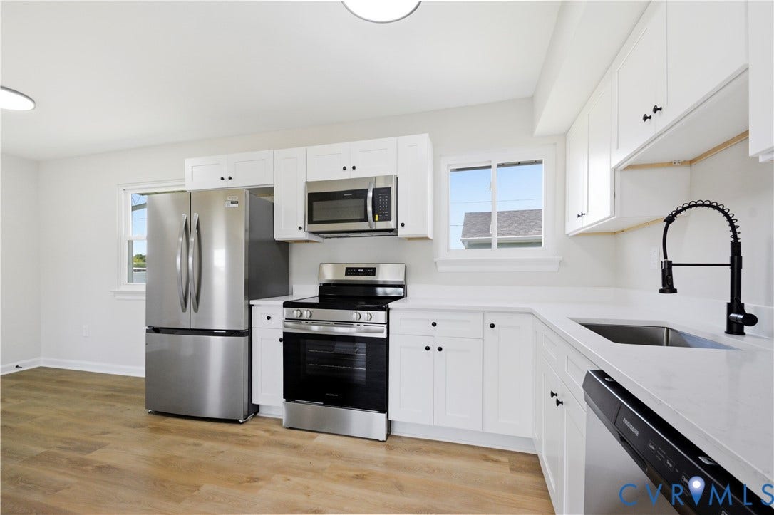 Kitchen featuring white cabinetry, stainless steel appliances, white countertops, a stainless steel sink with a black coiled faucet, and wood-finish flooring