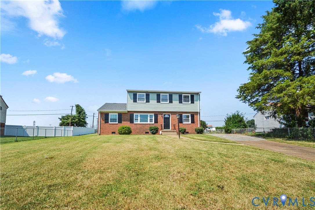 Brick and siding exterior with black shutters, mature tree, and expansive front lawn