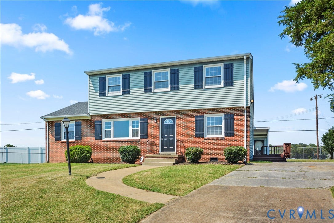 Two-story residence featuring brick and siding exterior, a front entry with storm door, dark shutters, a concrete driveway, and a paved walkway