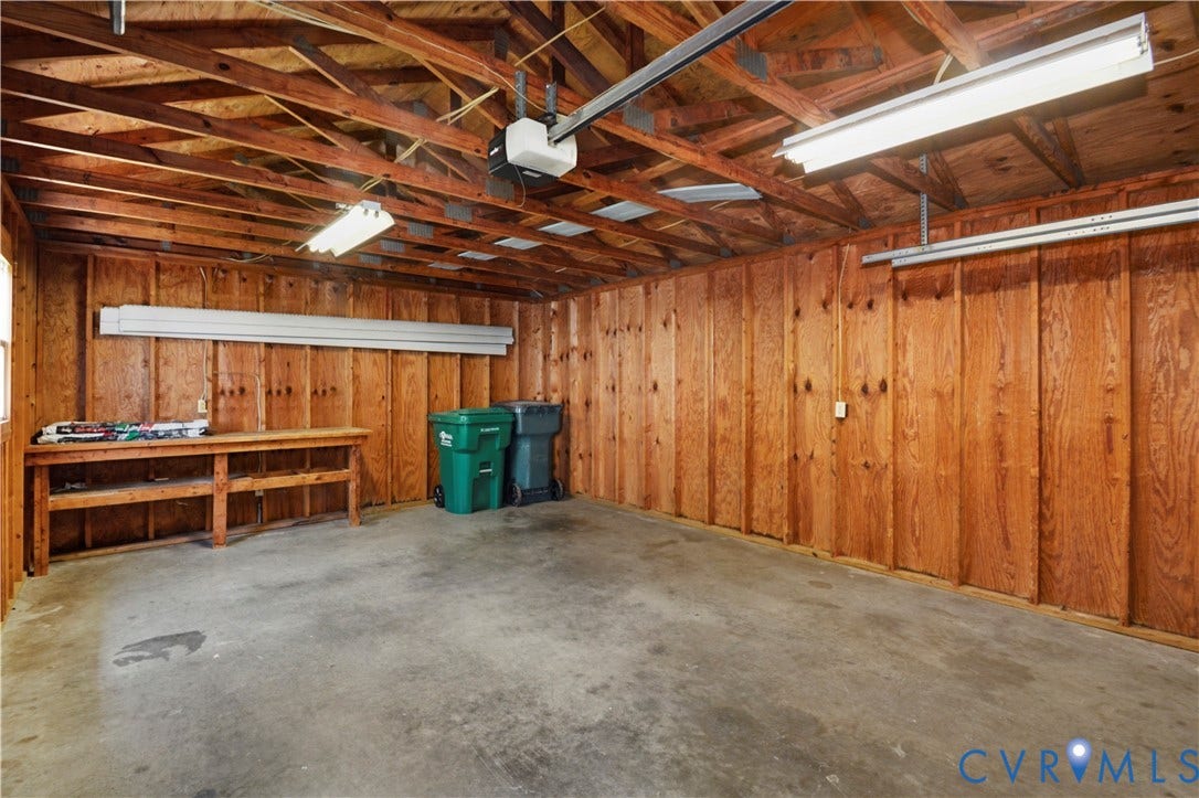 Concrete flooring, wood-paneled walls, exposed wood ceiling beams, built-in workbench, and overhead lighting