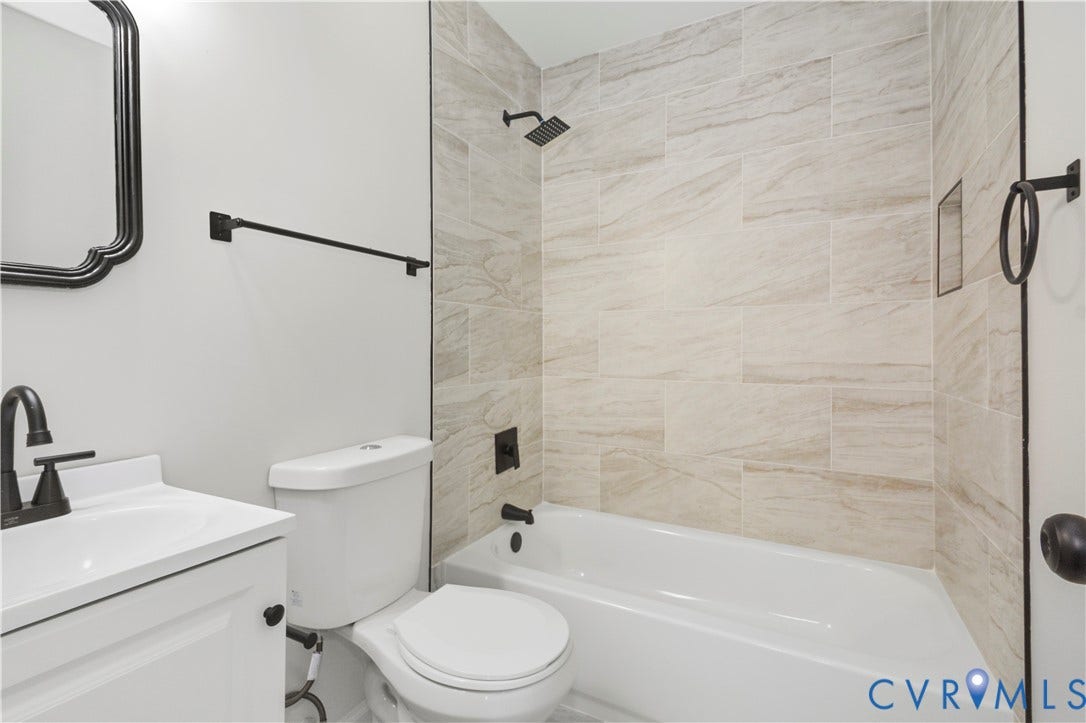 Bathroom featuring a white vanity with integrated sink, matte black fixtures, a white toilet, and tiled shower walls with an integrated niche