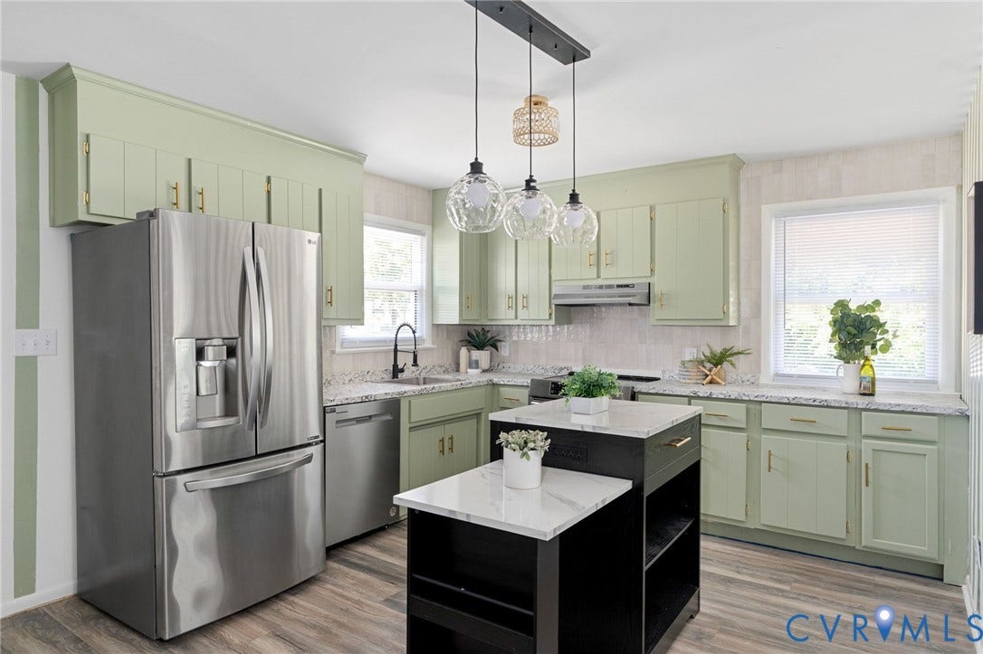 Kitchen featuring light green cabinetry, stainless steel appliances, a black kitchen island with a white countertop, and wood-finish flooring