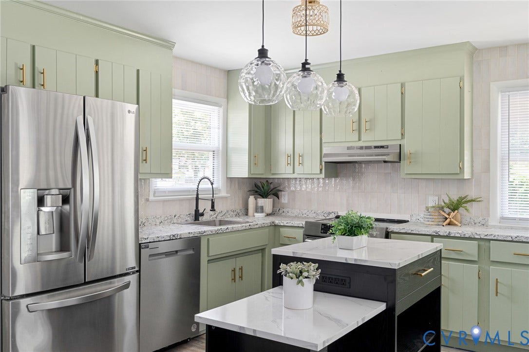 Kitchen featuring light green cabinetry with gold-tone hardware, white countertops, stainless steel appliances, and a central island with a white countertop