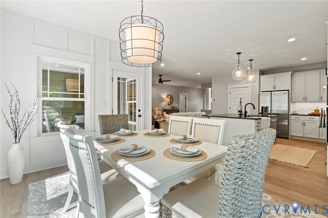 9143 Terroir Lane, Villas, New Kent, VA 23124 Open-concept living space with wood-finish flooring, white paneled wall accents, a dining area featuring a caged drum pendant light, and a kitchen with white cabinetry, dark countertops, and stainless steel appliances