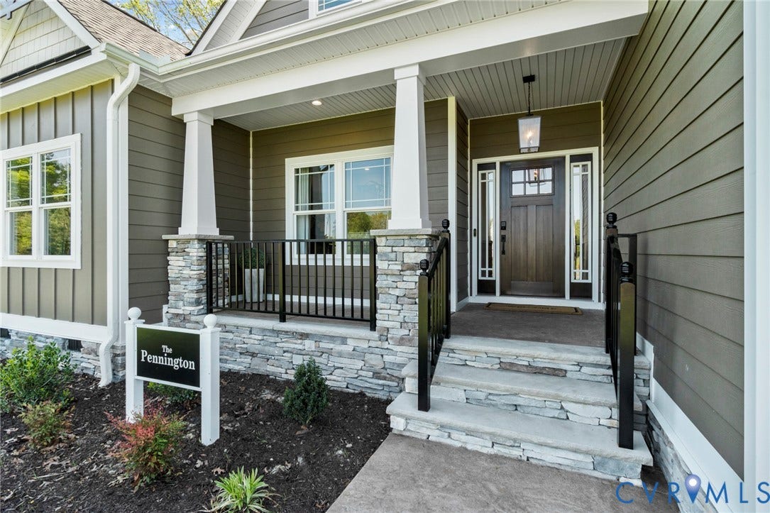 9143 Terroir Lane, Villas, New Kent, VA 23124 Stone veneer foundation and porch columns, dark wood-finish entry door with sidelights, white-framed windows, and a covered front porch with black railings