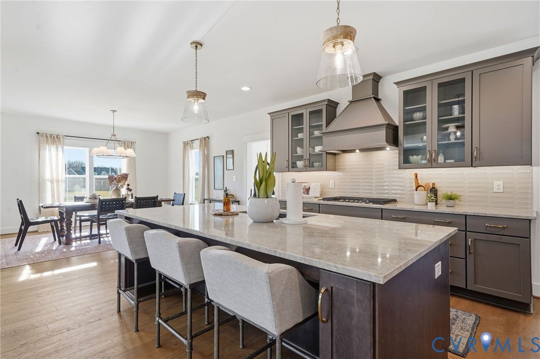 9169 Terroir Lane, Villas, New Kent, VA 23124 Kitchen featuring a large central island with seating, a built-in range with a modern hood, extensive cabinetry with glass-front uppers, light-toned countertops, and wood-finish flooring