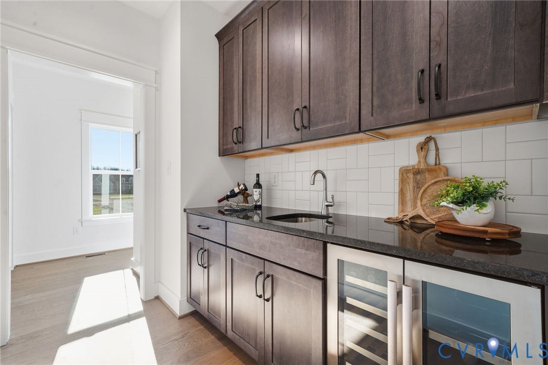 9169 Terroir Lane, Villas, New Kent, VA 23124 Built-in cabinetry with dark wood-finish, stone countertop, undermount sink, beverage cooler, and subway tile backsplash