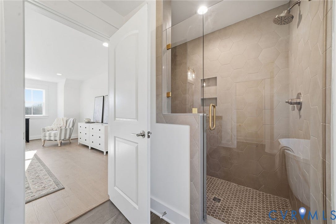 9169 Terroir Lane, Villas, New Kent, VA 23124 Glass-enclosed shower with hexagon wall tiles, contrasting penny tile flooring, recessed niche shelving, and a rain showerhead