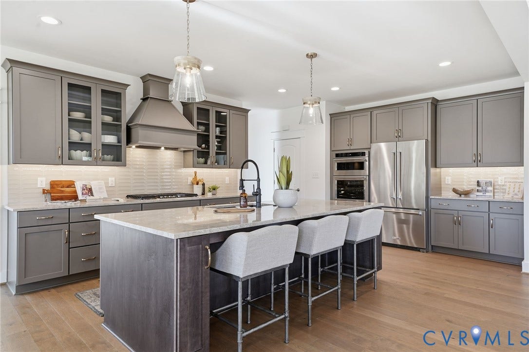 9169 Terroir Lane, Villas, New Kent, VA 23124 Gourmet kitchen featuring stainless steel appliances, a large center island with seating, grey shaker cabinetry, glass-front upper cabinets, and wood-finish flooring