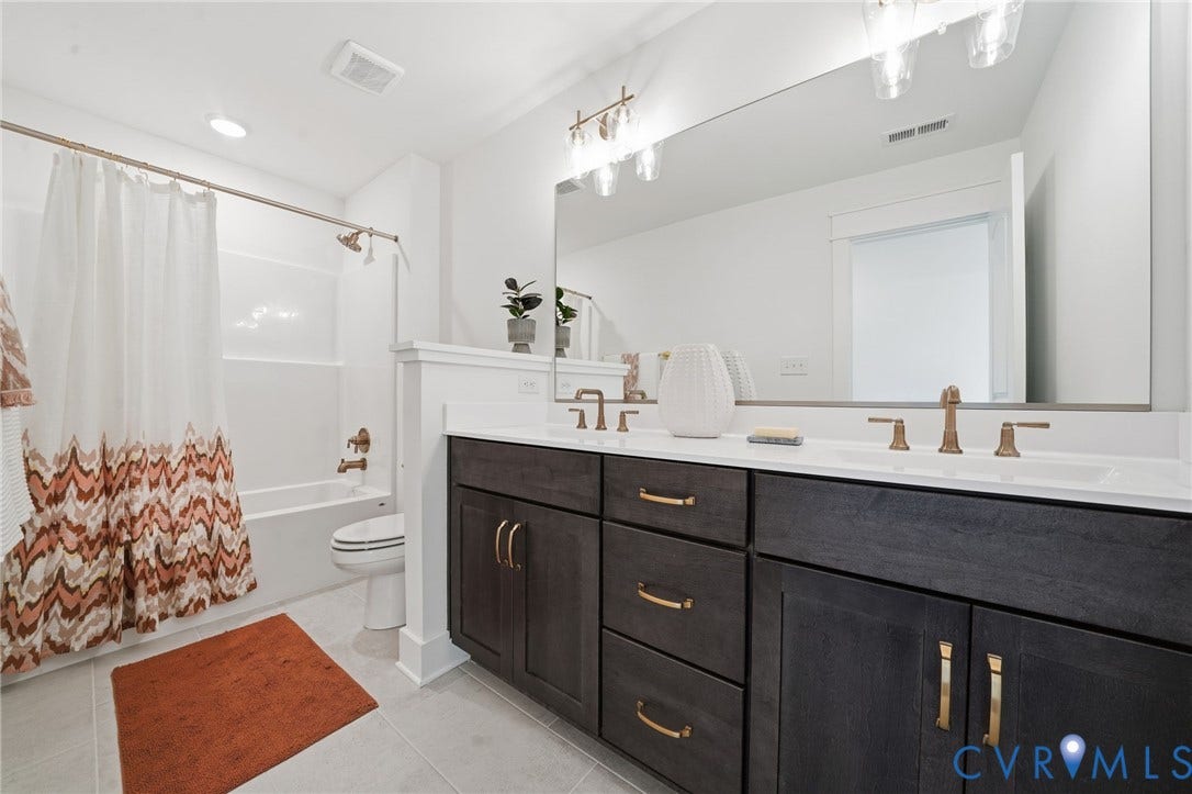 9169 Terroir Lane, Villas, New Kent, VA 23124 Dual vanity with integrated sinks, dark wood-finish cabinetry, brushed bronze hardware, and a full-width mirror