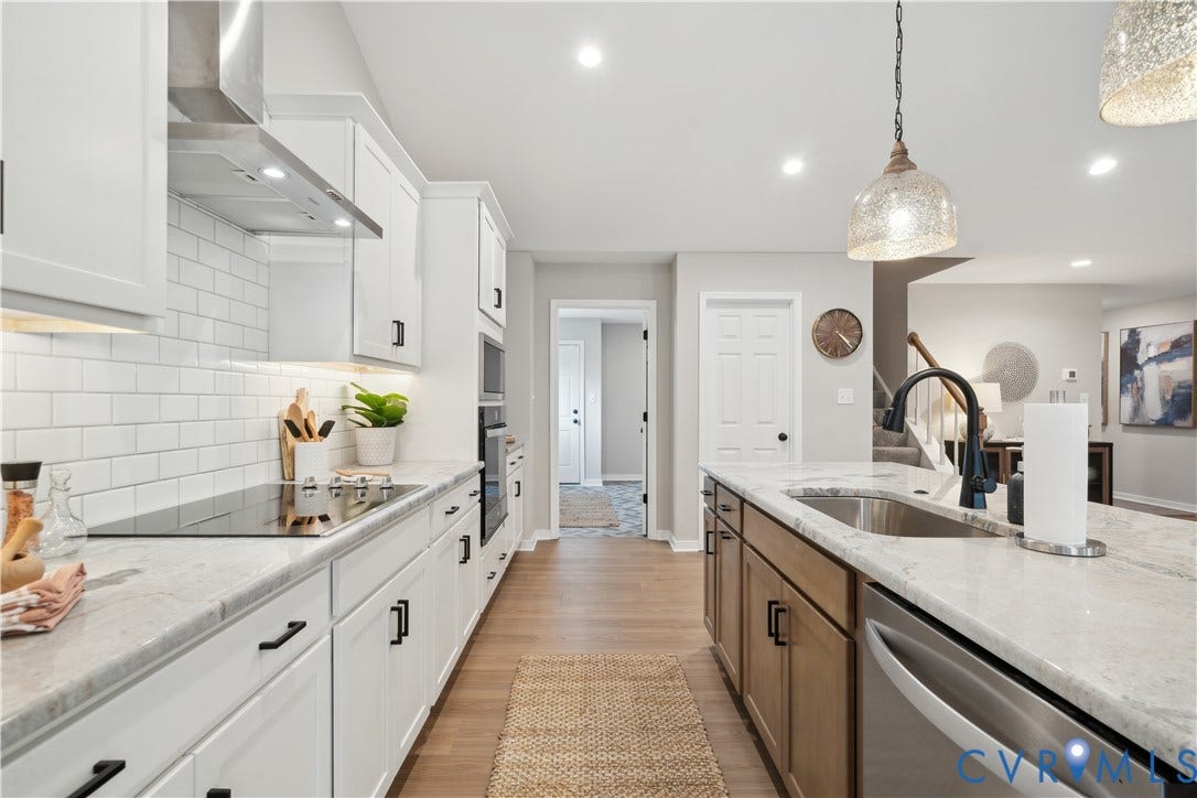 9102 Terroir Lane, Viniterra Villas, New Kent, VA 23124 Kitchen featuring white cabinetry with black hardware, white subway tile backsplash, stainless steel appliances, and a central island with an undermount sink