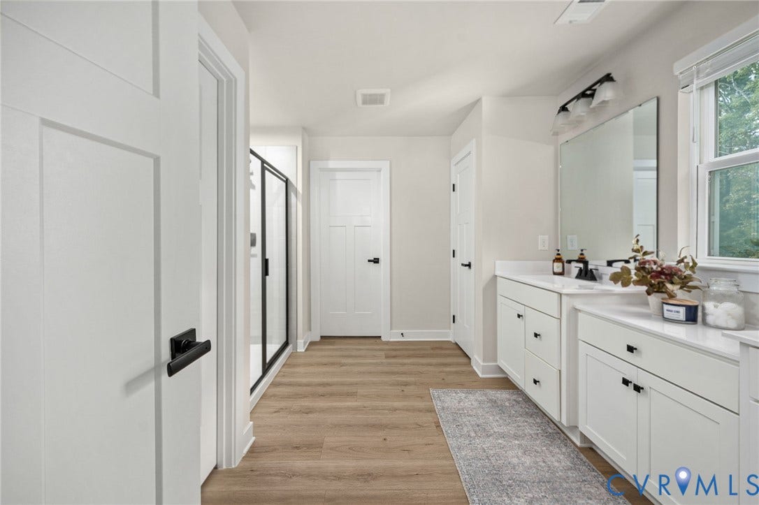 1961 Enon Station Drive, Chester, VA 23836 Dual vanities with white cabinetry, wood-finish flooring, a glass-enclosed shower, and a large window