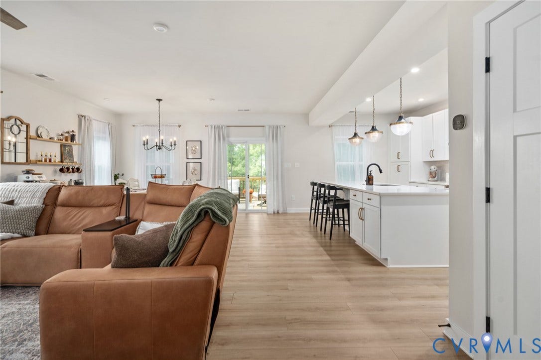1961 Enon Station Drive, Chester, VA 23836 Open-concept living space featuring wood-finish flooring, white kitchen cabinetry, a kitchen island with seating, pendant lighting, and a sliding glass door