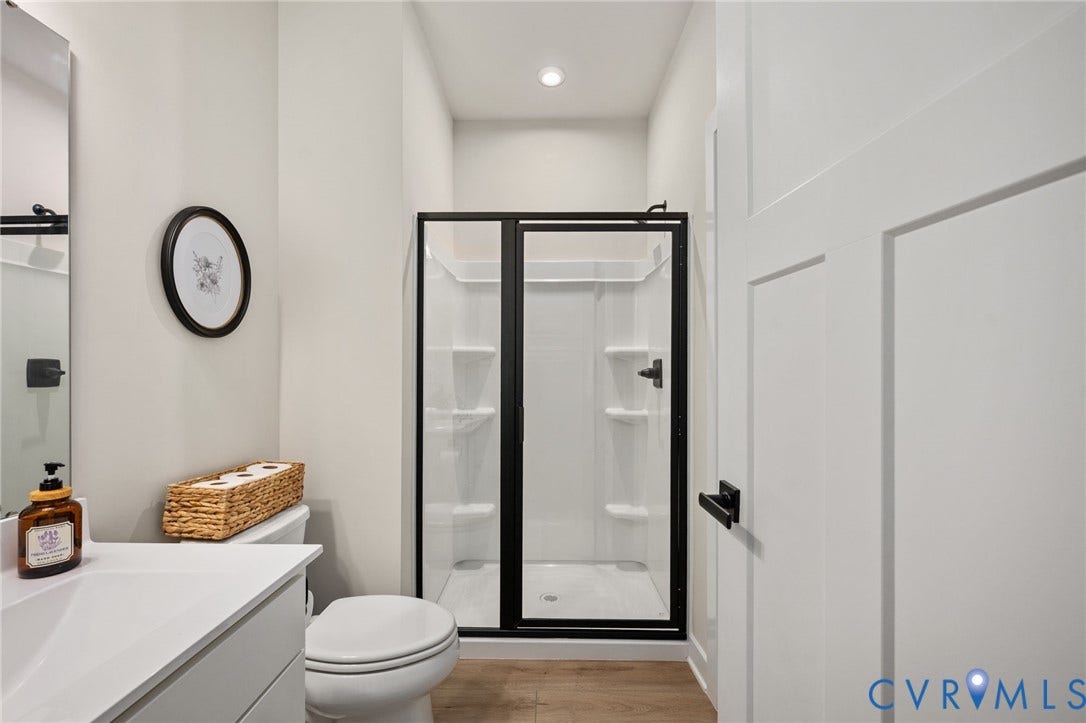 1961 Enon Station Drive, Chester, VA 23836 Wood-finish flooring, white vanity with integrated sink, black-framed glass shower, white toilet, and recessed lighting