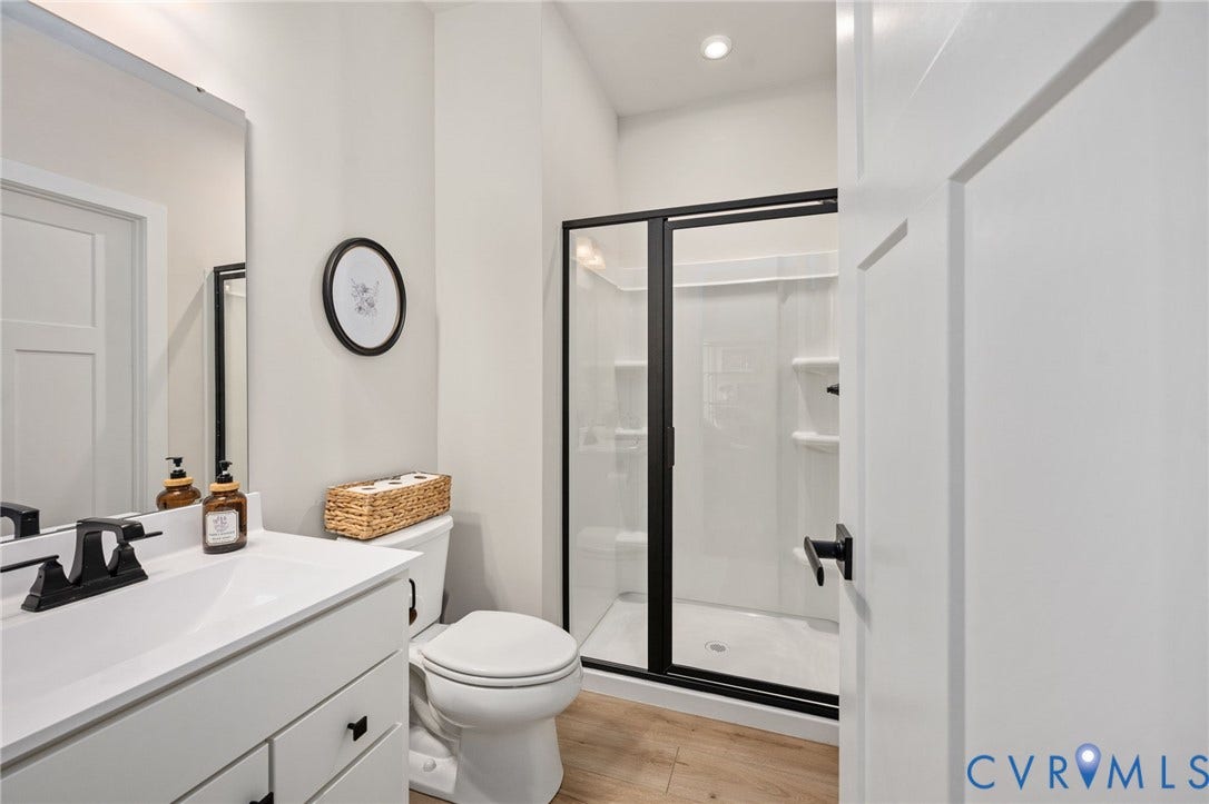 1961 Enon Station Drive, Chester, VA 23836 White vanity with a single sink and matte black faucet, glass-enclosed shower with matte black framing, wood-finish flooring, and recessed lighting