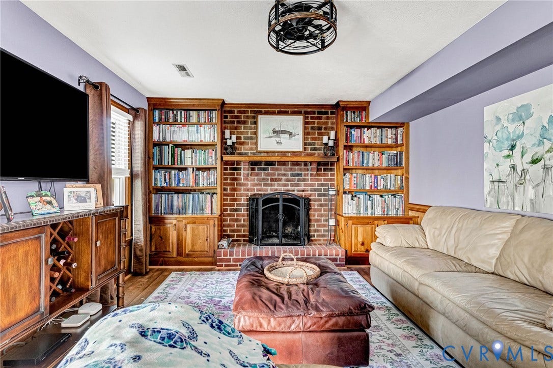 Brick fireplace with a metal screen, flanked by built-in wood shelving units, hardwood flooring, and a decorative ceiling fan