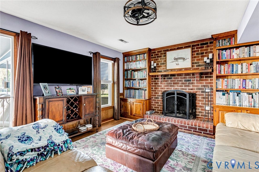 Brick fireplace with a wood mantel, built-in shelving, and wood-finish flooring